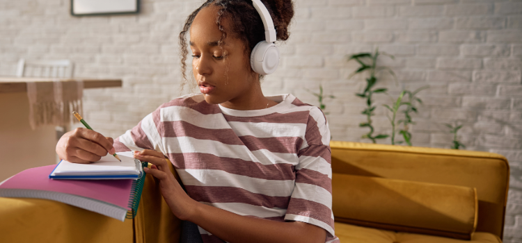 Flicka med hörlurar pluggar i gul soffa