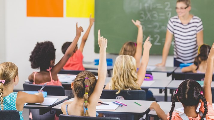 Barn i ett klassrum som räcker upp händerna.