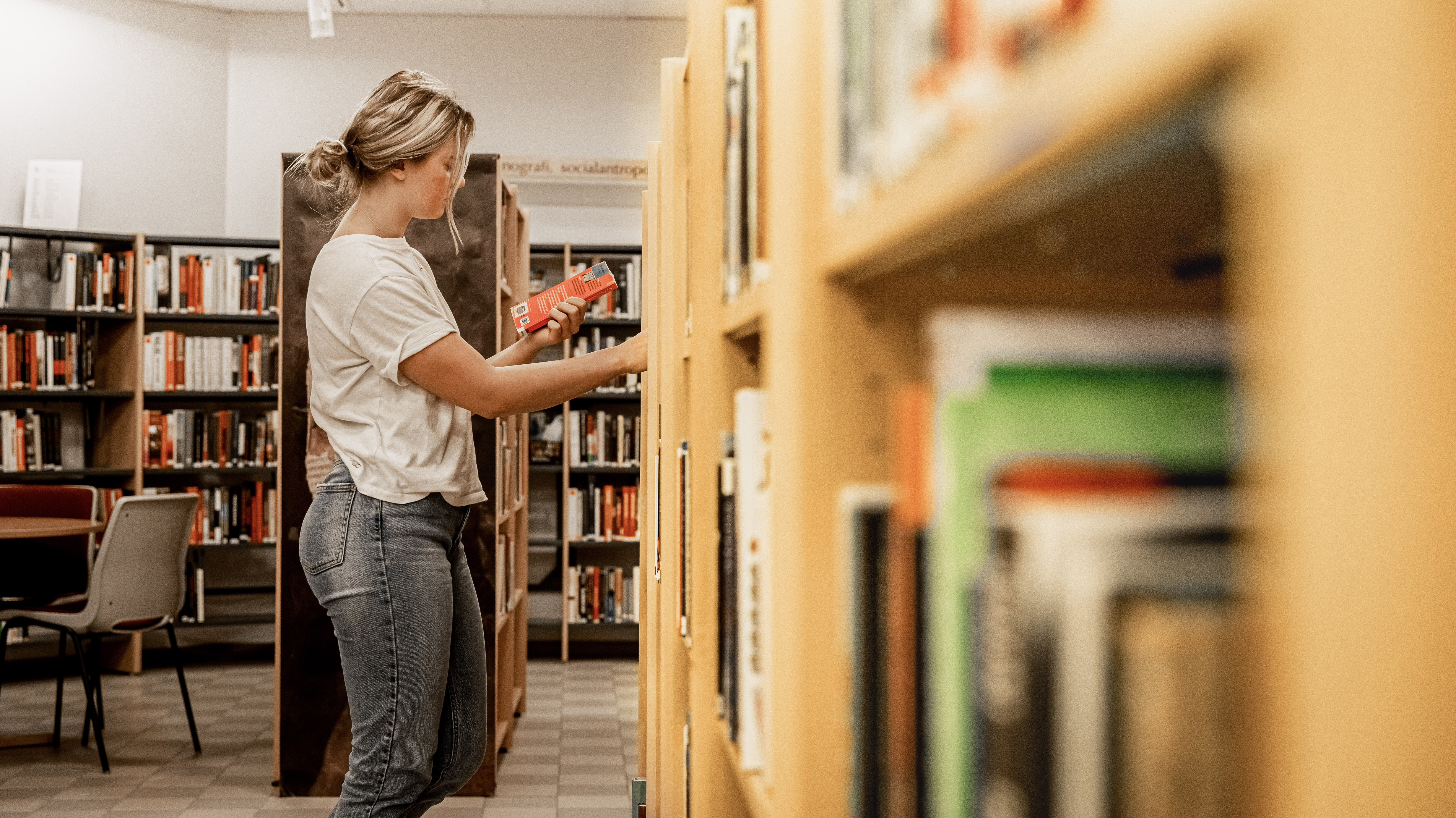 Tjej håller i en bok ståendes vid bokhylla